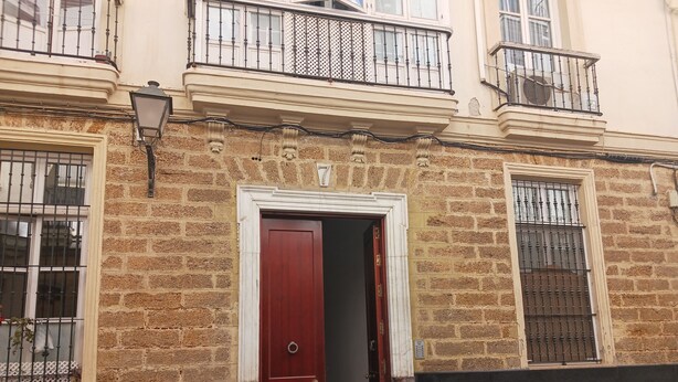 A building with a red door, brick facade, and barred windows. - Habitación Privada con Cuarto de Baño (Cádiz)