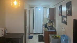 A narrow hallway with a dining area on one side and a kitchenette on the other. There is a hanging light fixture, a curtain, and a water dispenser on the right. - Songeza Furnished Accomoda-super Studio,embakasi (Nairobi)