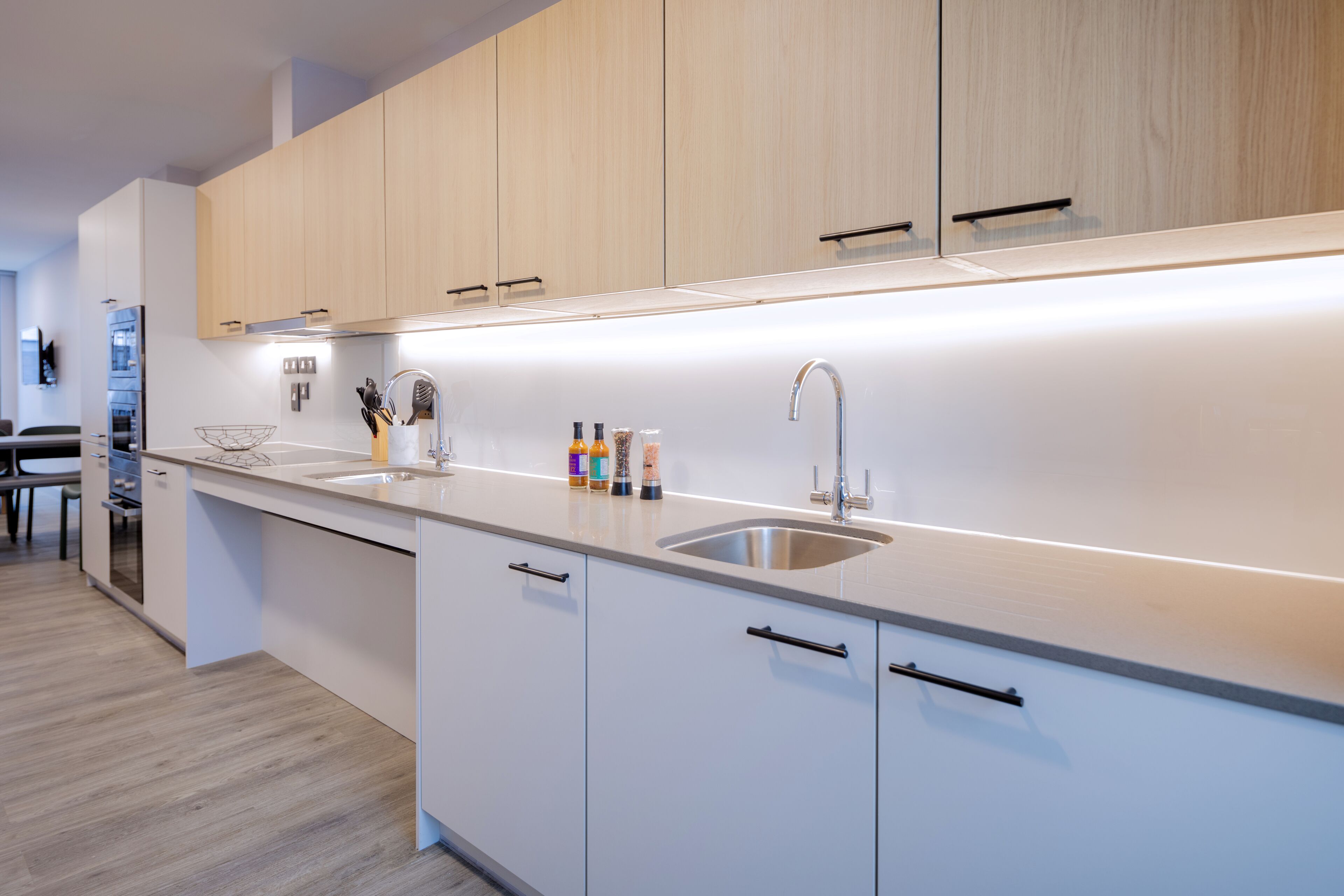 A modern kitchen with light wood cabinets, a stainless steel sink, and a countertop with various items.