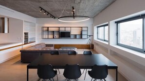 A modern living space with a large sofa, a dining table with chairs, a mounted TV, and a large window with a city view. - Athens Market Iconic Loft, Stunning Acropolis View (Athens)