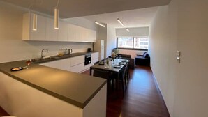 A modern kitchen with white cabinets, a central island, and a dining area with a long table. - Athens Market Iconic Apartment, Amazing view of the Acropolis (Athens)