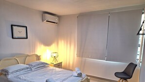 A bedroom with a bed, bedside lamp, air conditioning unit, window with blinds, and a chair. - Lindo y moderno apartment in lovely Samborondon with WiFi, AC (Guayaquil)