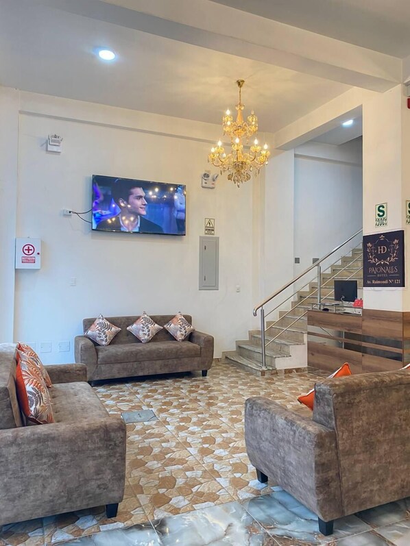 Een hotelhal met een zithoek, een kroonluchter, een televisie en een trap.