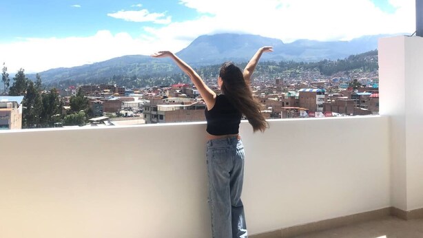 A person standing on a balcony with arms raised, overlooking a cityscape with mountains in the distance. - Hotel Los Pajonales (Huaraz)