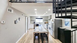 A modern kitchen with a central island, a dining area with a table and chairs, and a staircase leading to an upper level. - Modern Industrial House + Guesthouse in Midtown (Phoenix)
