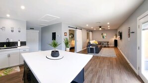 A modern kitchen with a central island, a dining area with a sofa and table, and a living space with a TV and plants. - Modern Industrial House + Guesthouse in Midtown (Phoenix)
