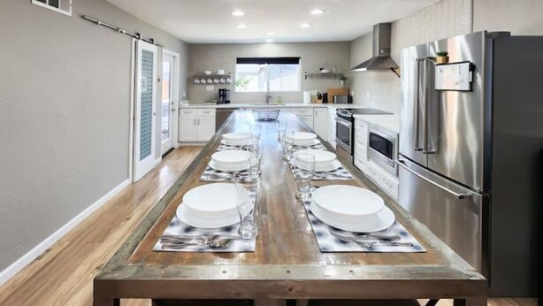 A modern kitchen with a long dining table set for six, stainless steel appliances, and a view of the outdoors. - Modern Industrial House + Guesthouse in Midtown (Phoenix)