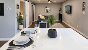 A dining area with a table set for four, a potted plant, and a sofa in the background. - Modern Industrial House + Guesthouse in Midtown (Phoenix)
