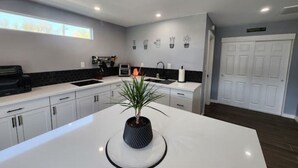 Una cocina moderna con armarios blancos, una isla central con planta en maceta, un microondas y una cafetera.
