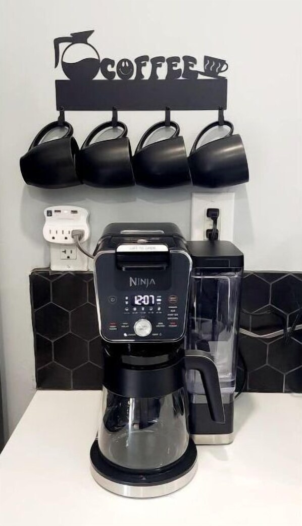 Une machine à café posée sur un plan de travail blanc, avec une cafetière noire et un écran numérique.