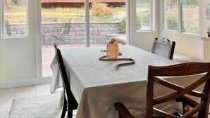 Ein Essbereich mit Tisch für zwei Personen, einem Holzstuhl und Blick in den Garten durch große Fenster.