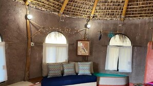 A rustic room with a thatched roof, a sofa with patterned cushions, a small table, and a framed picture on the wall.