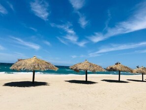 Una playa con sombrillas de paja y un cielo azul despejado.