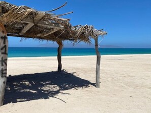 Una playa con una estructura de techo de paja, agua azul cristalina y arena dorada.