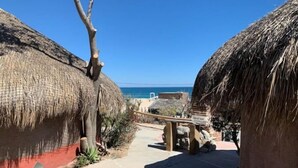 A pathway leading to thatched-roof huts with a view of the sea. - Casita Vista: Ocean Views, Private Hot Tub & You! (Buenavista)
