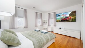Une chambre moderne avec un lit, un téléviseur diffusant une publicité pour une voiture et une commode blanche.