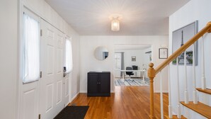 Un couloir avec un plancher en bois, des portes blanches, un meuble noir, un miroir et un escalier doté d’une rampe en bois.