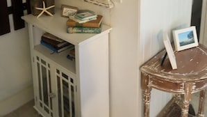 Una habitación con un espejo rústico, una pequeña mesa con un marco de fotos y un aparador con libros y adornos.