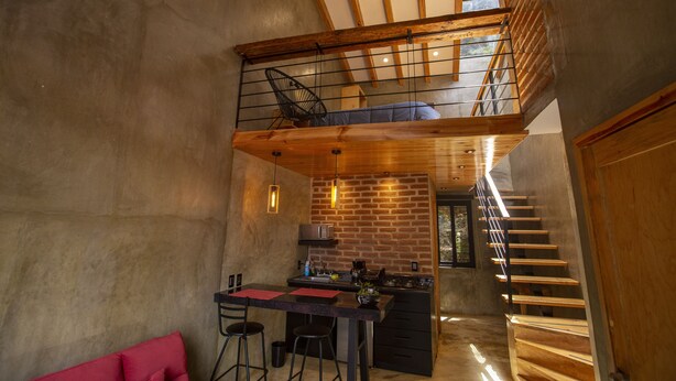 Una cocina moderna con pared de ladrillo, vigas de madera y un entresuelo con una silla.