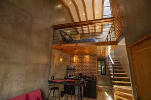 A modern kitchen with a brick wall, wooden beams, and a mezzanine with a chair. - Casa Don Pedro Faro (San Cristóbal de las Casas)