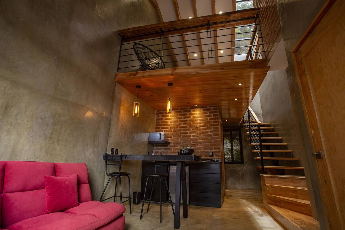 A modern interior with a red sofa, a kitchen area, and a staircase.