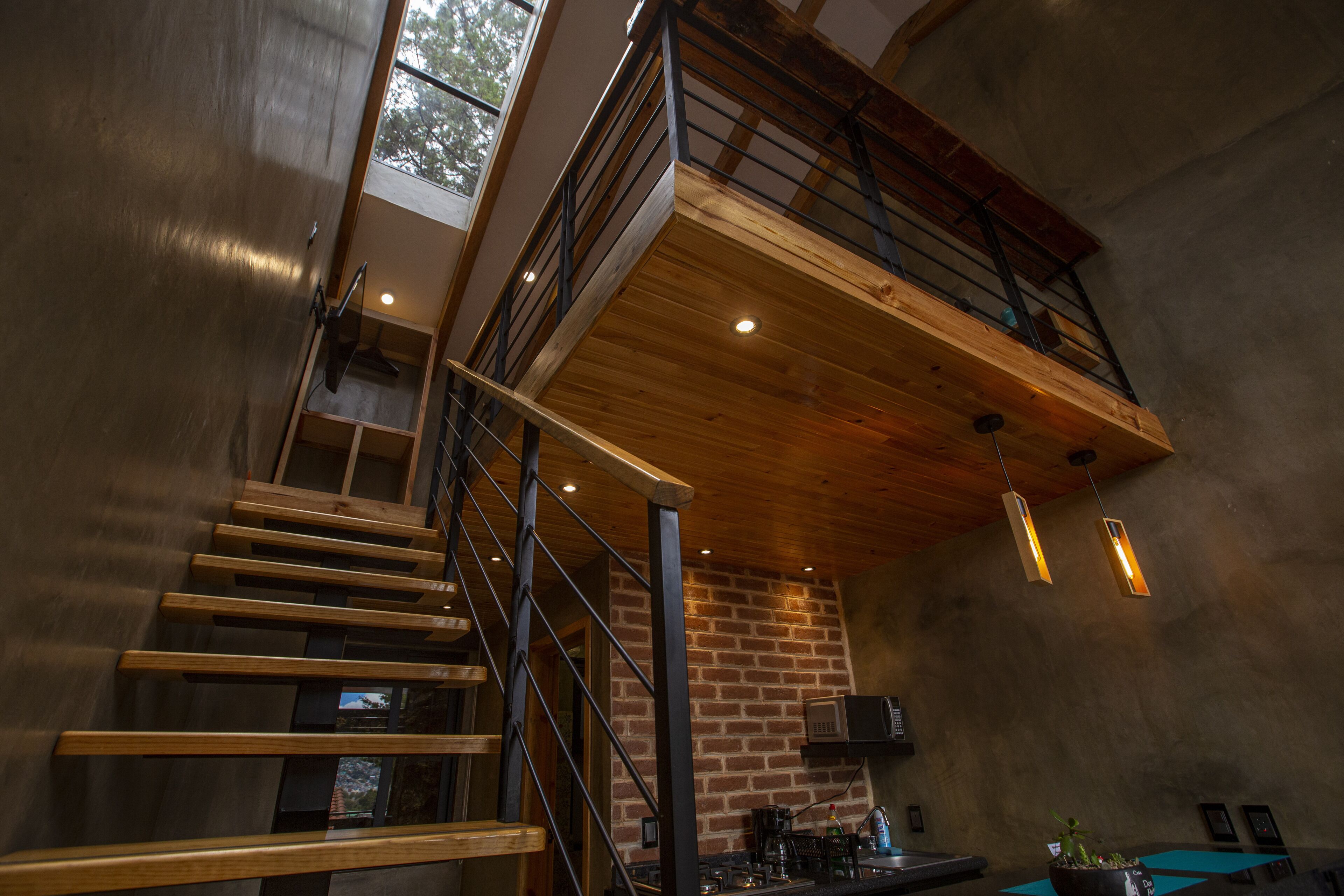 A modern interior with a wooden staircase, a brick wall, and a mezzanine level.