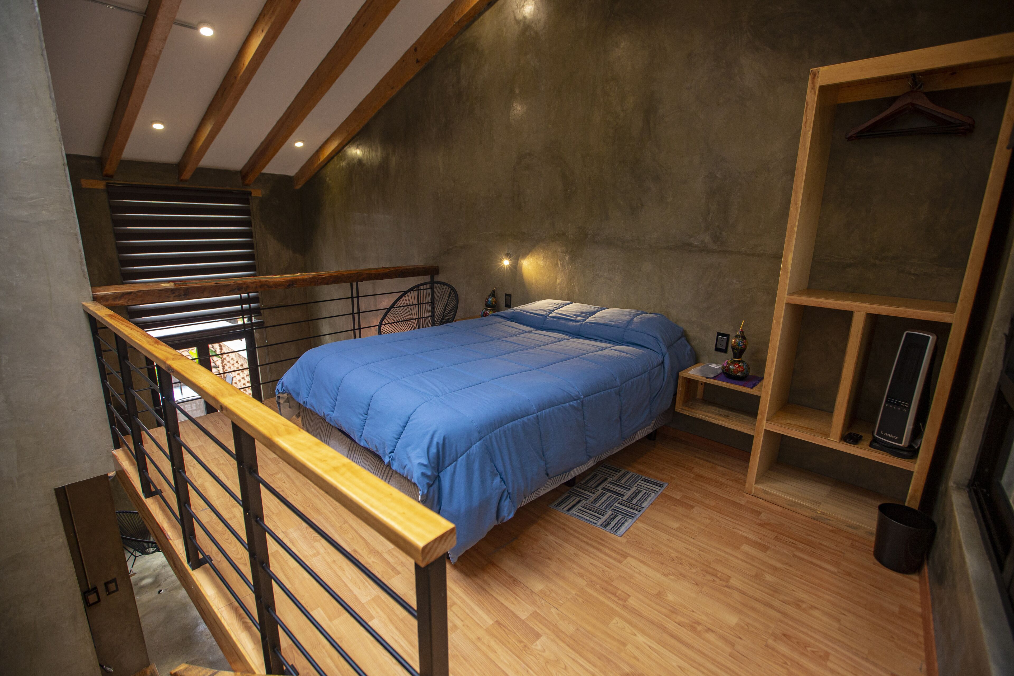 Une chambre à coucher avec un lit, un plancher en bois, un fauteuil suspendu, une petite table et une étagère avec un haut-parleur.
