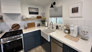 Une cuisine moderne avec des meubles blancs, une cuisinière en acier inoxydable, un lave-vaisselle et un évier placé sous une fenêtre.