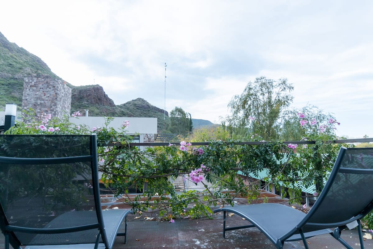Una terraza en la azotea con dos sillones de descanso, vistas a un paisaje montañoso y un edificio con fachada de piedra.