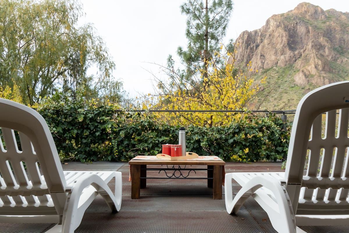 Un patio con dos sillas blancas, una mesa de madera y una caja roja.