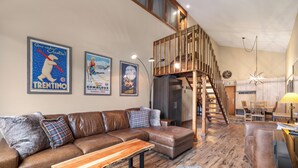 A spacious living room with a brown leather sofa, a wooden coffee table, and a staircase leading to an upper level.