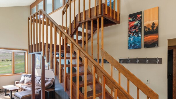 A wooden staircase with glass railings leading to an upper floor. There is a couch and a small table in the lower area.