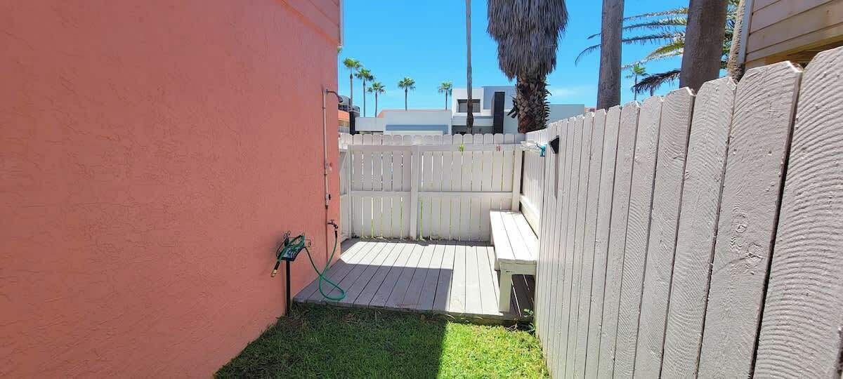 A fenced backyard with a wooden deck, a grassy area, and a hose.