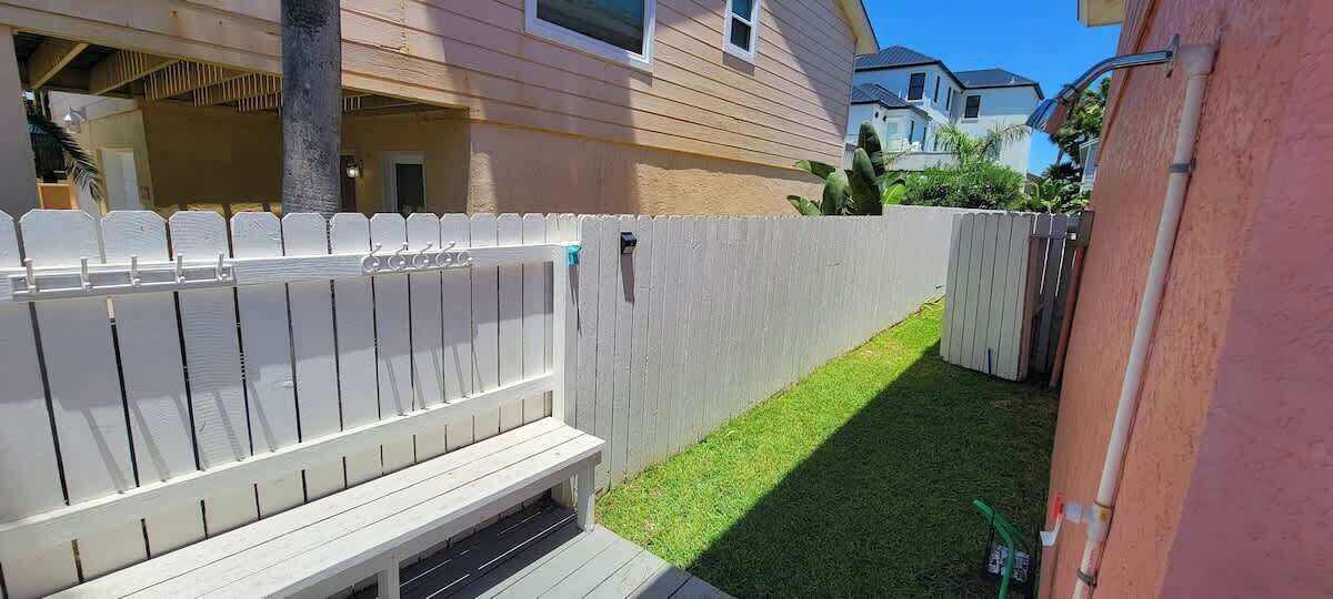 A fenced backyard with a wooden bench and a small patch of grass.