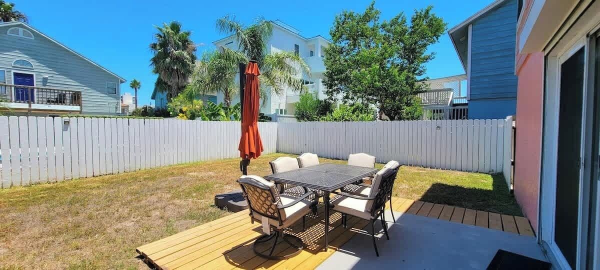 A backyard with a wooden deck, a dining table with chairs, and a red umbrella.