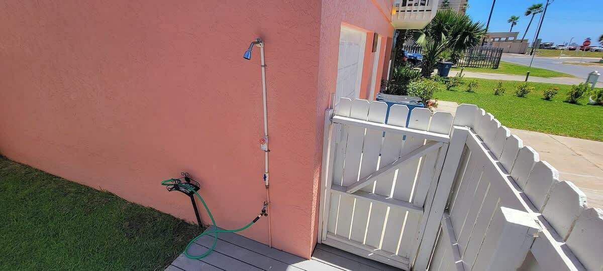 A gated entrance with a white picket fence, a hose attached to the wall, and a door with a window.