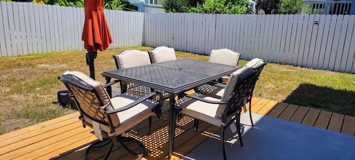 Une terrasse avec une table et des chaises, entourée d’une clôture blanche.