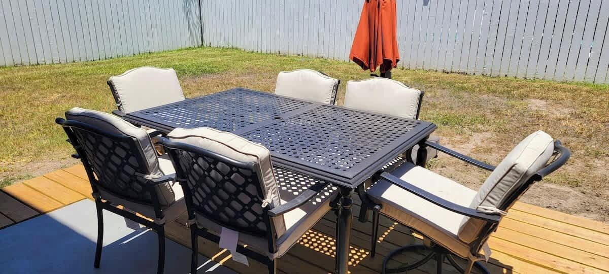A patio with a metal table and chairs, a wooden deck, and a fence in the background.