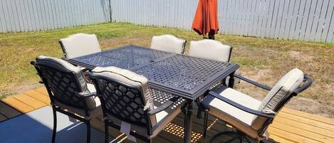 A patio with a metal table and chairs, a wooden deck, and a fence in the background.