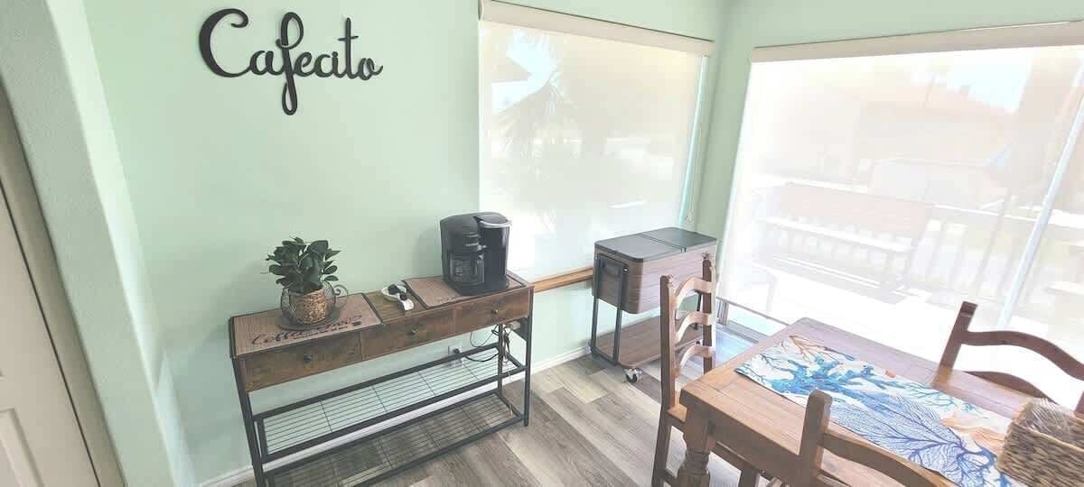 A cafe area with a coffee machine, a small table, chairs, and a wall-mounted sign that reads 'Cafe'.