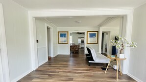 A hallway with a wooden floor, white walls, and a seating area with a sofa and a small table. There are framed pictures on the walls and a potted plant on the table. - Relaxing Water view Onset Beach 3 bedrooms walking distance to everything (Wareham)