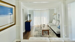 A spacious living area with a sofa, a coffee table, and a TV. There is a painting on the wall and a window with curtains. - Relaxing Water view Onset Beach 3 bedrooms walking distance to everything (Wareham)