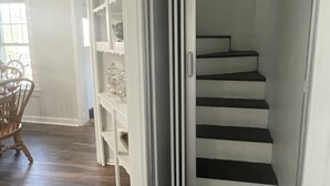 A staircase with white steps and a glass door leading to a room with a wooden floor and a dining area with chairs and a table. - Relaxing Water view Onset Beach 3 bedrooms walking distance to everything (Wareham)