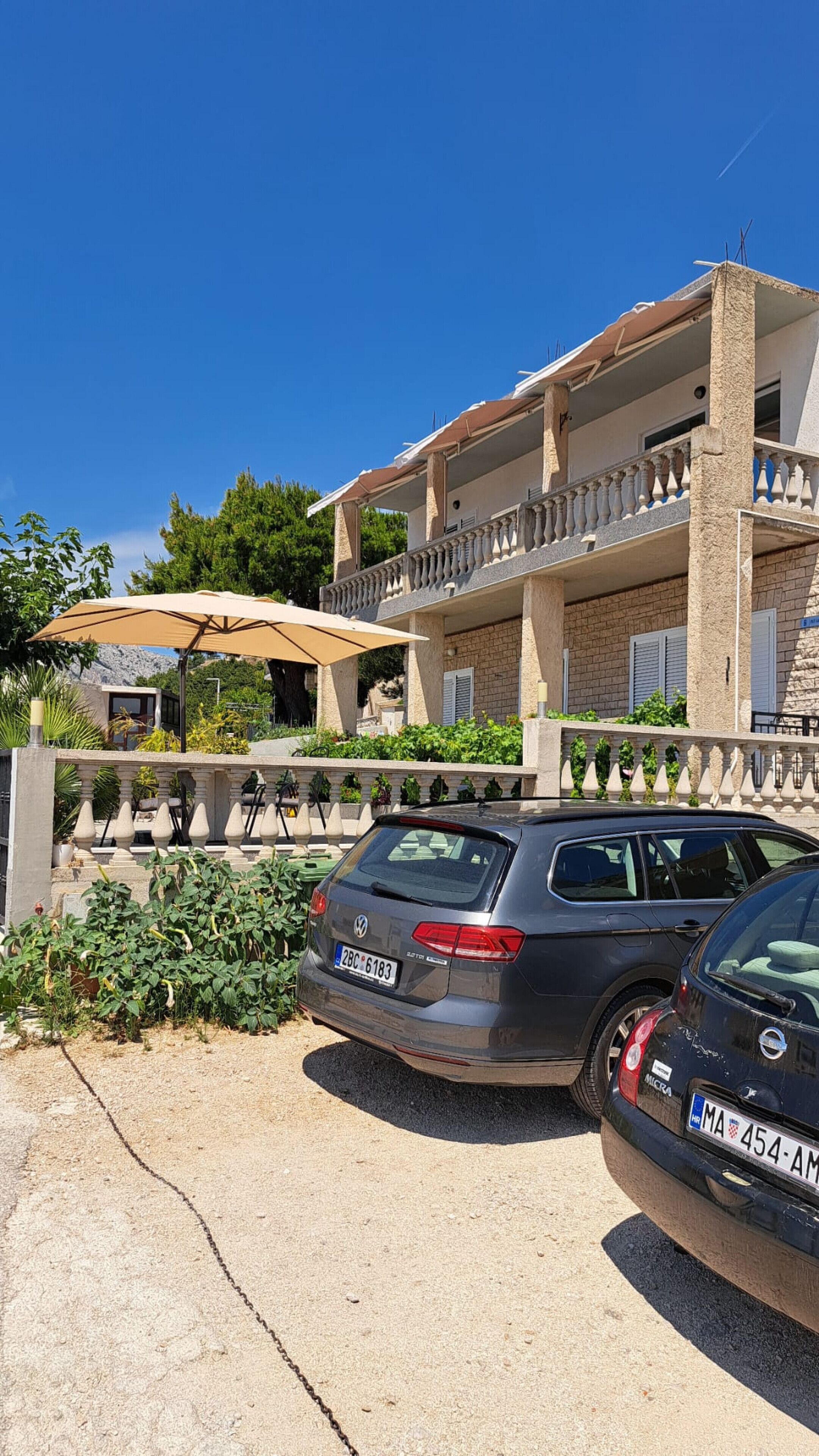 A two-story building with a balcony, parked cars, and a clear blue sky.
