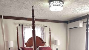 Ein Bett mit Baldachin, mit roter Bettdecke, zwei Nachttische mit Lampen, ein Teppich mit Blumenmuster und eine Deckenleuchte.