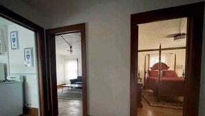 Ein Zimmer mit einem Bett, einem Schreibtisch und einem Stuhl. Eine Tür führt in einen weiteren Raum.