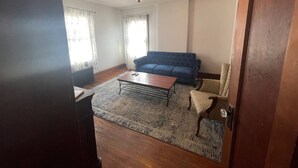 Ein Wohnzimmer mit einem blauen Sofa, einem Holztisch und einem gemusterten Teppich.