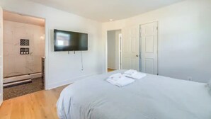 Un dormitorio moderno con una cama grande, un televisor de pantalla plana montado en la pared y una zona de ducha con puerta de cristal.