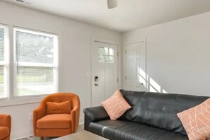 Un salon moderne avec un canapé en cuir noir, un fauteuil orange et une porte dotée de panneaux en verre dépoli.