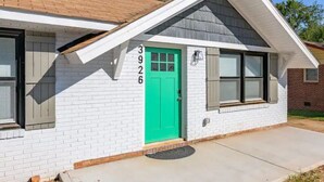 Una casa de un piso con puerta verde, fachada de ladrillo blanco y un pequeño porche.